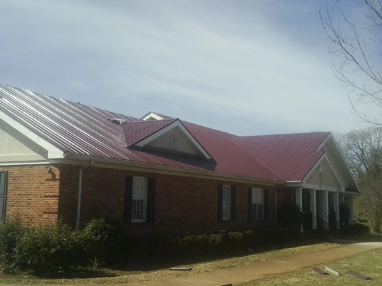 Red metal roof with gabled entries on a long brick building, from a Hail Damage Roof Repair job in Christiansburg