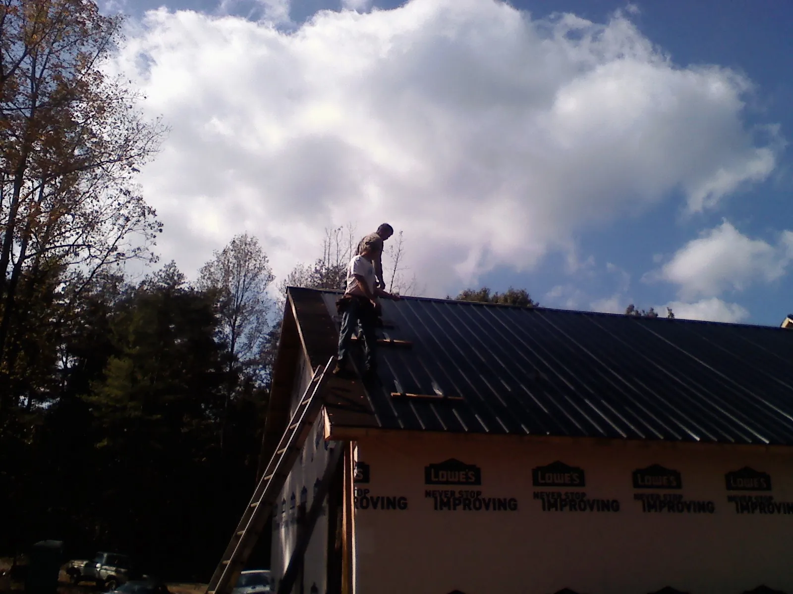Roofer fastening dark metal panels high against a cloudy sky, from a Roof Inspection job in Christiansburg