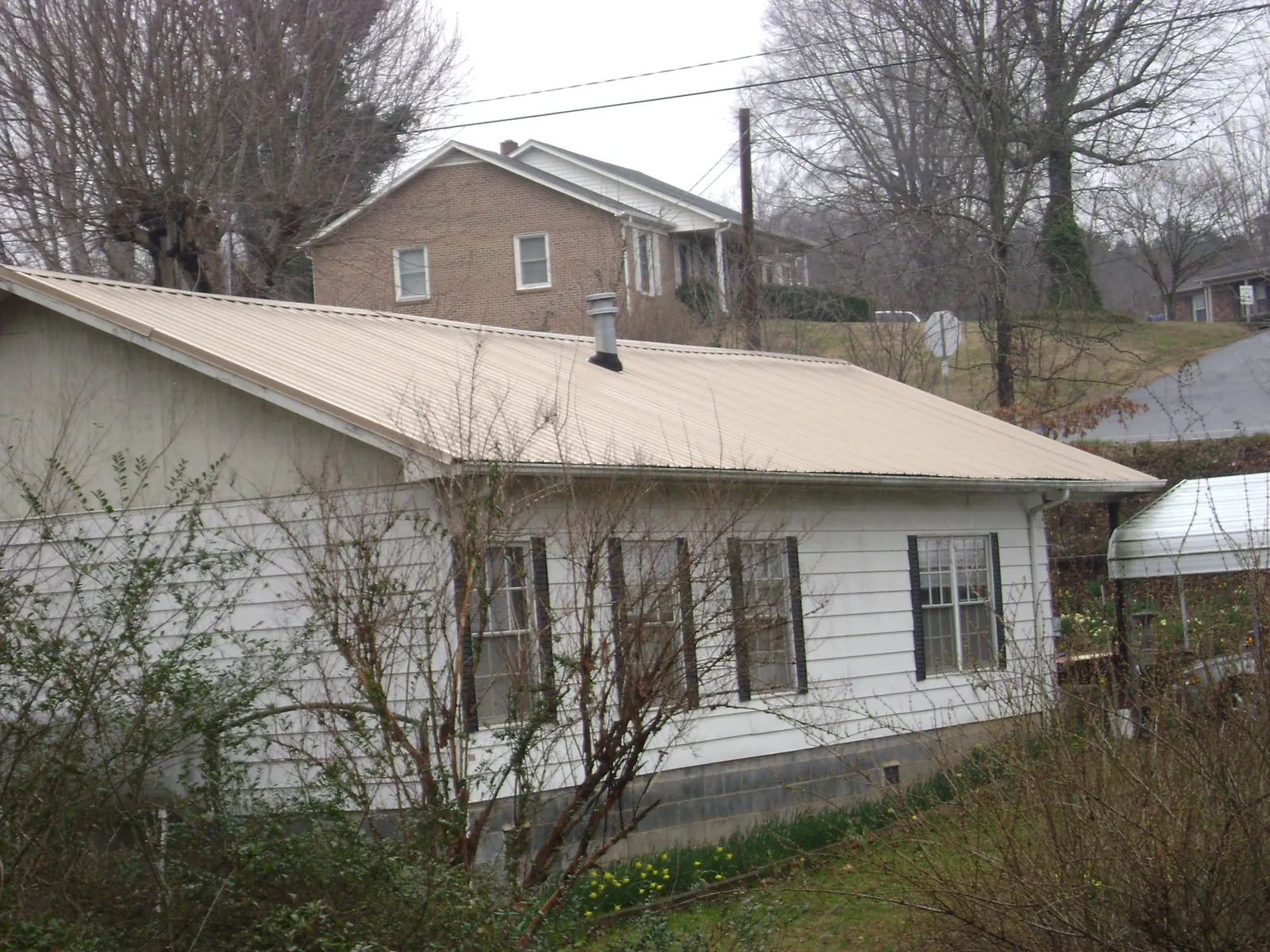 Tan metal roof on a white sided house set into a hillside — Commercial Roofing by Roofing Brothers in Christiansburg